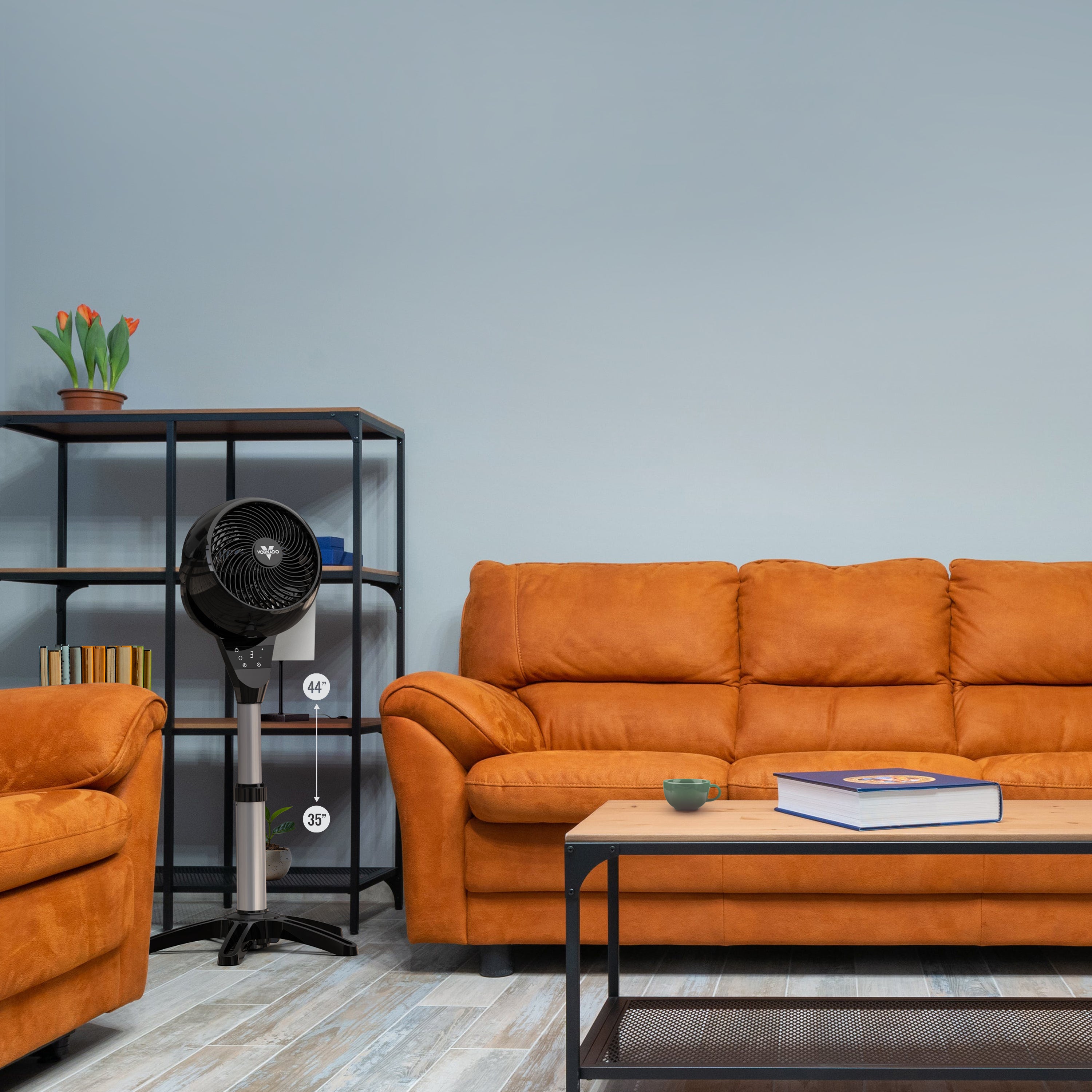 Vornado oscillating pedestal fan in a living room setting, showing its adjustable height and compact footprint for whole-room air circulation.