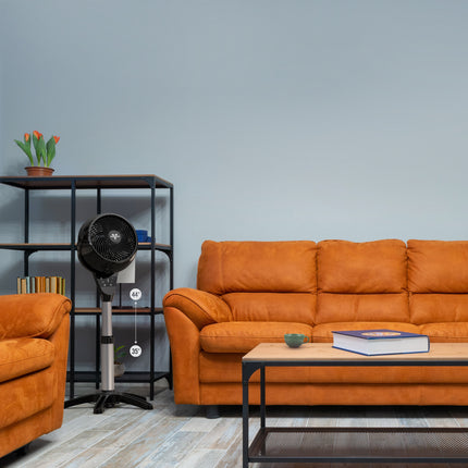 Vornado oscillating pedestal fan in a living room setting, showing its adjustable height and compact footprint for whole-room air circulation.