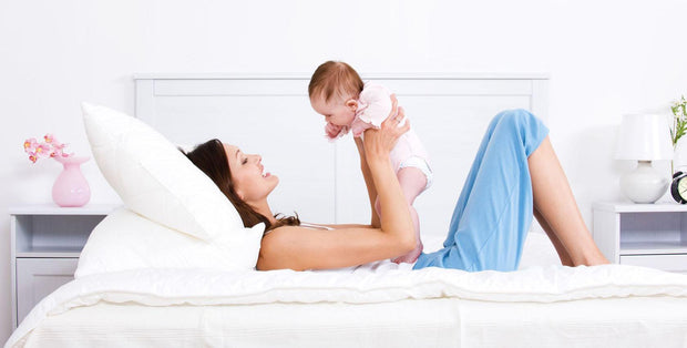 A mother and her baby laying on a bed.