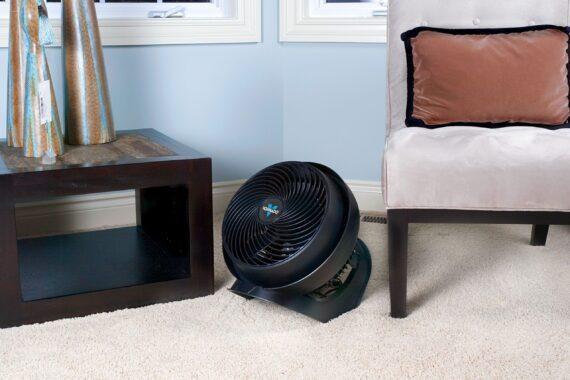 Lifestyle of a Black 733 large air circulator on a carpeted floor by a chair and small table