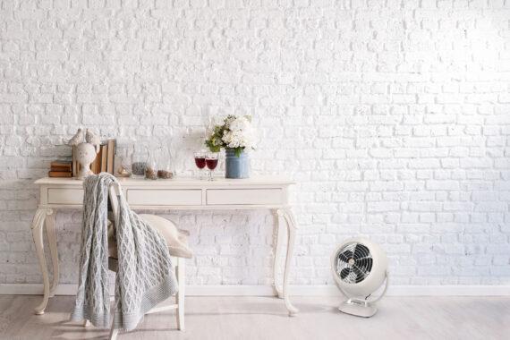Lifestyle of a white vintage VFAN air circulator by a desk and white brick wall