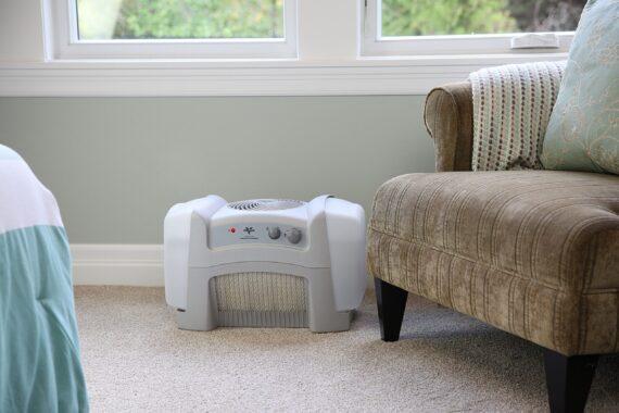 Lifestyle of a white evap40 evaporative humidifier on a carpeted floor by a window and chair