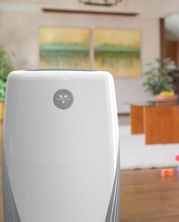 Lifestyle of a PCO575DC air purifier with a blurred living room in the background.