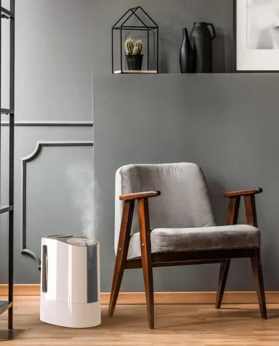 Lifestyle of a UH100 humidifier misting near a chair and wood side table in a living room.