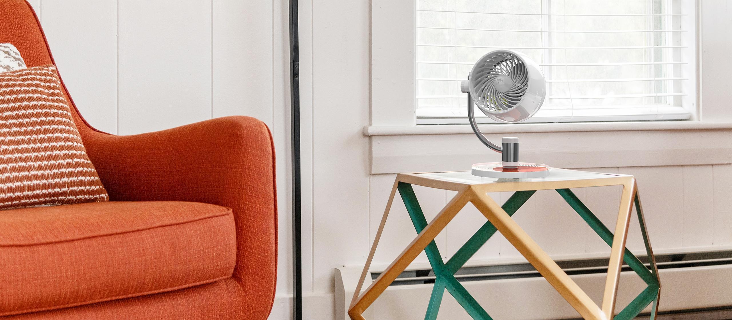 Pivot3U Compact Air Circulator on a abstract coffee table with geometric legs. There is a bright red sofa next to the table.