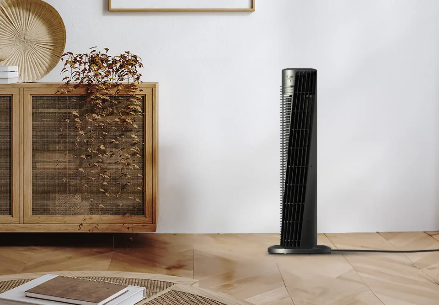 Lifestyle image of OSC54 tower fan. The fan is in a room with a grey wall, wood floor and a wicker cabinet and coffee table. The tower fan's cord goes off to the right, indicating it is plugged in