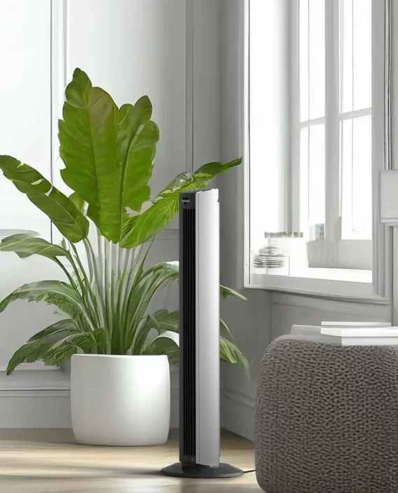 Lifestyle image of OZI42DC tower fan by a white wall, green plant and a window.