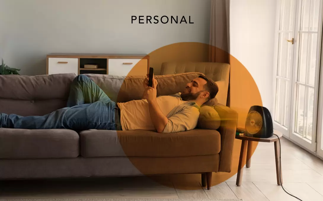 Man laying on a couch with the MVH heater on a side table. There is an orange circle overlay on him to indicate personal heat space.