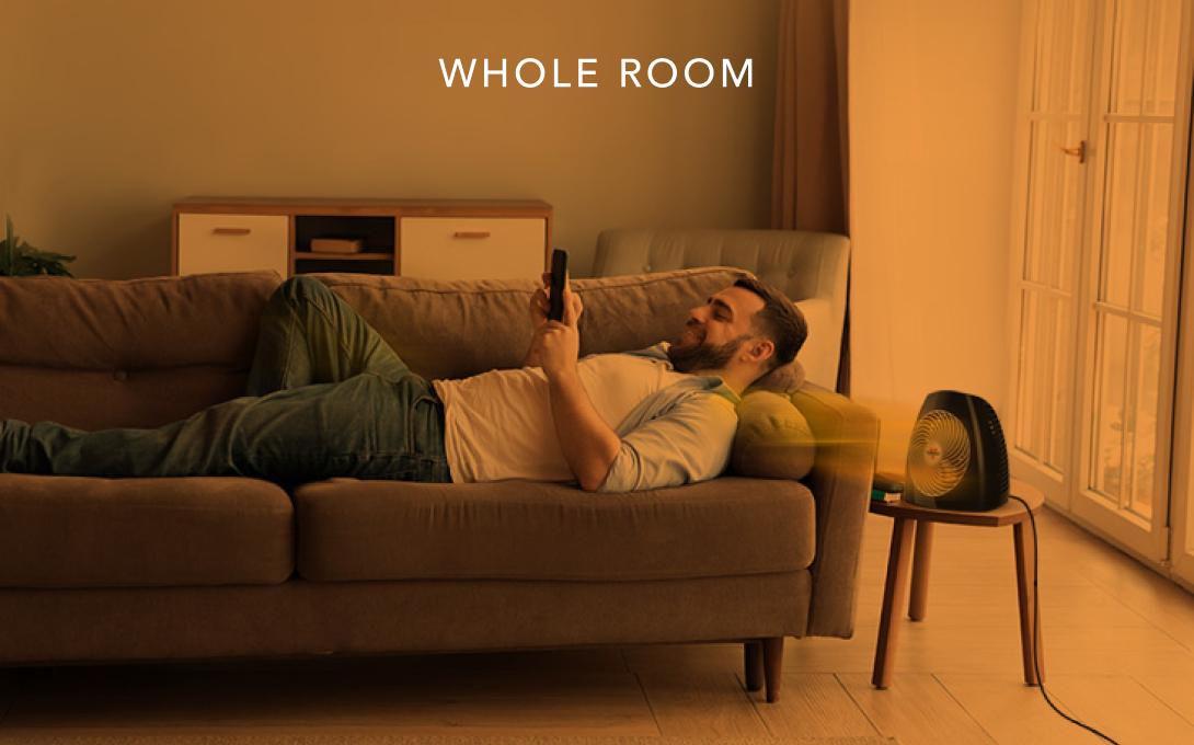 Man laying on a couch with the MVH heater on a side table. There is an orange overlay to indicate whole room heat.