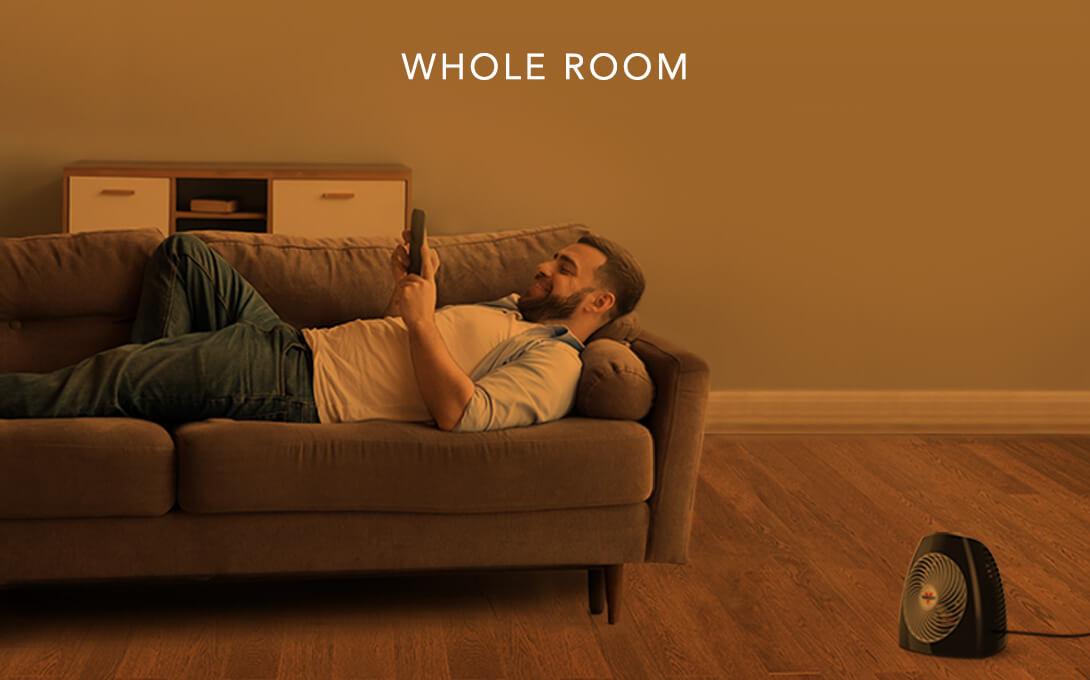 Man laying on a couch with the MVH heater on the floor. There is an orange overlay to indicate whole room heat.