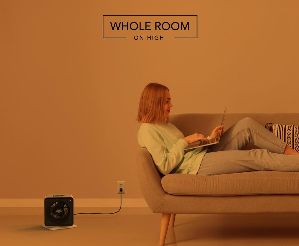 Woman laying on a couch with the Velocity Cube 5S heater on the floor. There is an orange overlay to indicate whole room heat on high.