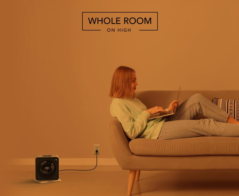 Woman laying on a couch with the Velocity Cube 5S heater on the floor. There is an orange overlay to indicate whole room heat on high.